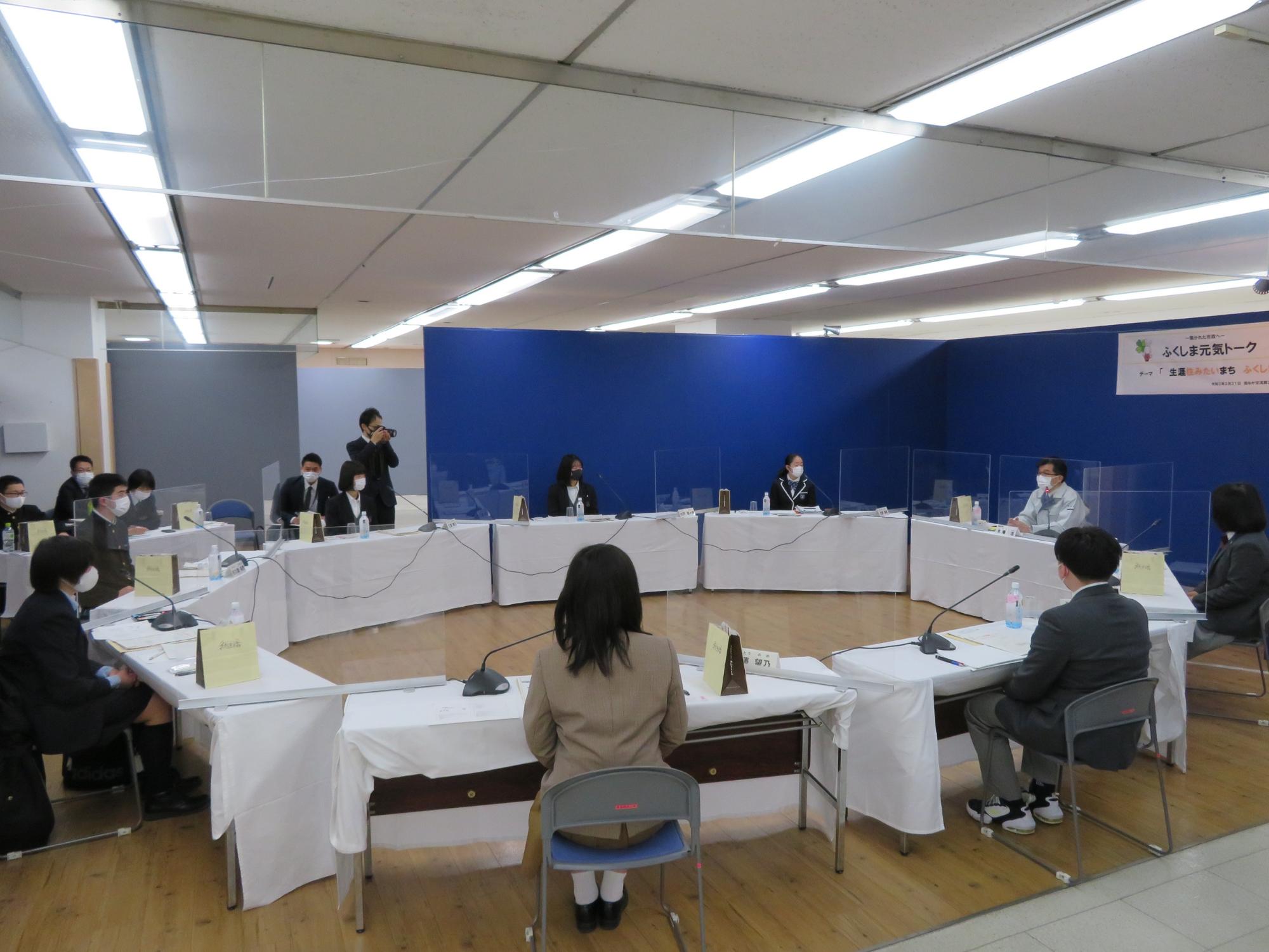 円形に並べられた机に、市長と関係者が椅子に座って意見交換を行っている写真