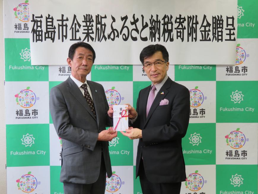 「福島市企業版ふるさと納税寄附金贈呈」の幕が貼られたバックパネルの前で、男性と市長で目録を持っている写真