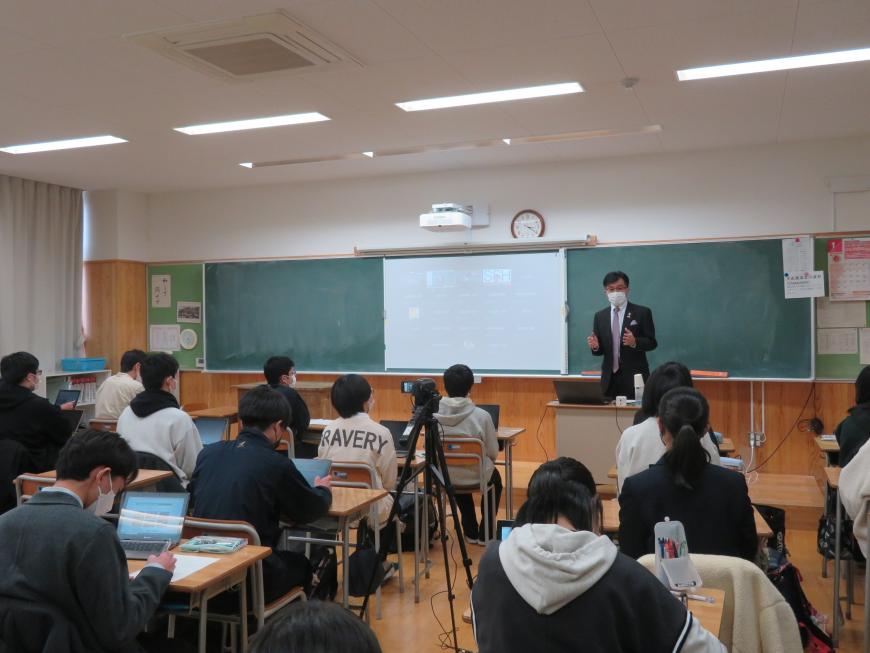 学校の教室で、生徒の前で市長が黒板に設置してスクリーンに画像を映し出しながら話をしている写真