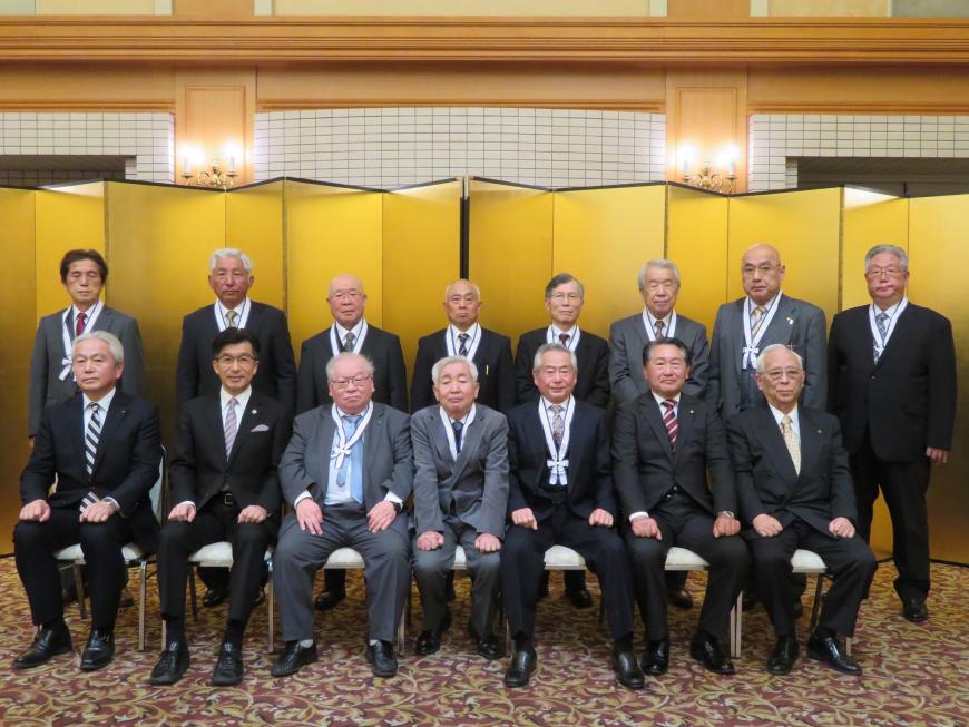 金屛風の前で前列に市長を含めた7名の男性が座り、後方に8名の男性が立っている記念写真
