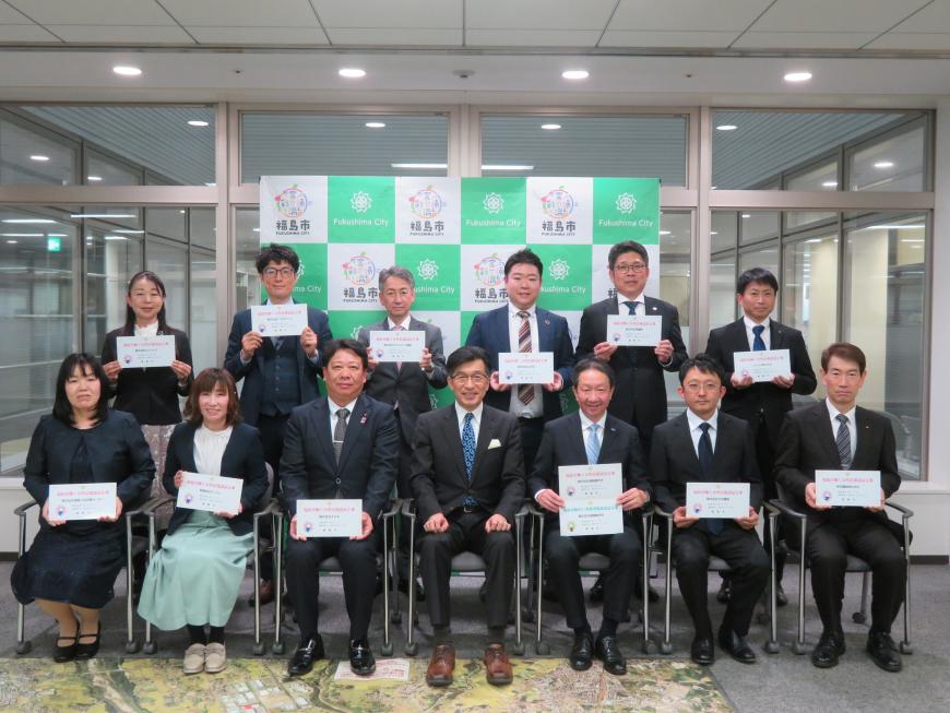 前列に市長を中心に女性2名と男性4名が座り、後方に女性1名、男性5名が立ち、それぞれ認定の書類をもっている写真