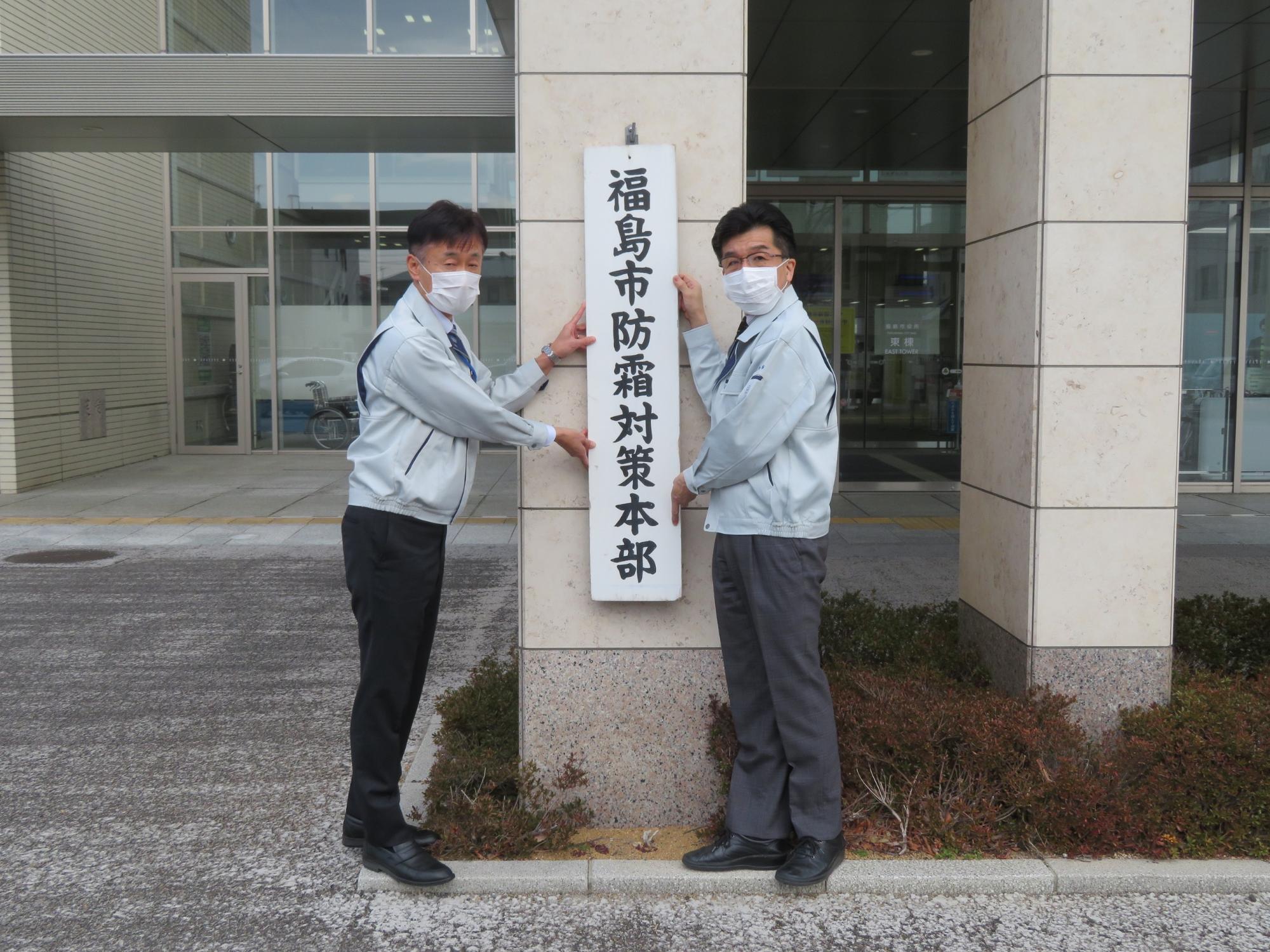 福島市防霜対策本部と書かれた看板を市長と男性で立てかけようとしている写真