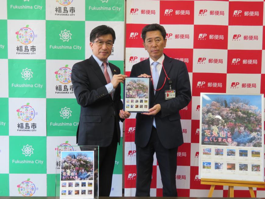 切手の拡大パネルが置かれている福島市と郵便局のバックパネルの前で、市長と男性で切手シートを持っている写真