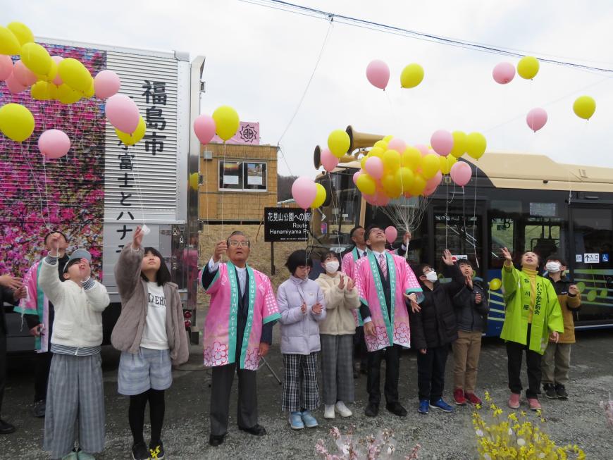 法被を着た市長と児童たちが横一列に並んでピンクや黄色の風船を飛ばしている写真