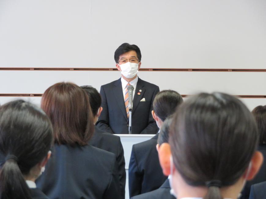 前方で市長がマイクを使い話しているのを新規採用職員の方々が聞いている写真