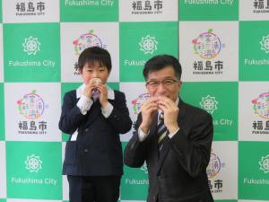 バックパネルの前で、制服姿の児童と市長がおむすびを食べている写真