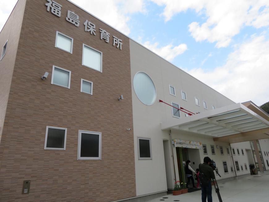 「福島保育所」と切り文字看板があり、大小の四角い窓や丸い窓が設置され、玄関に屋根がつけられた茶色とベージュの色の建物の写真
