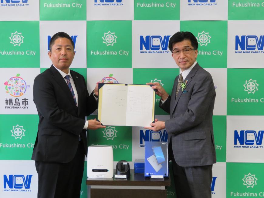 株式会社NCVと福島市のバックボードの前で市長と関係者の男性が協定書を一緒に持ち記念撮影している写真