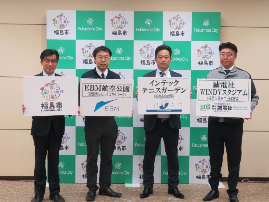 バックパネルの前で、市町が「福島市」、男性3名がそれぞれ「EBM航空公園」「インテックステニスガーデン」「誠電社WINDYスタジアム」と書かれたボードを持って立っている写真