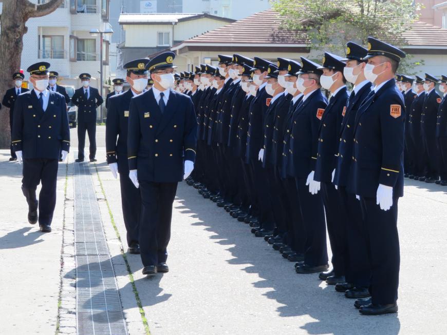 消防隊員が制服と帽子をかぶって整列し、その前を制服を着用した市長が歩いて点検をしている様子の写真