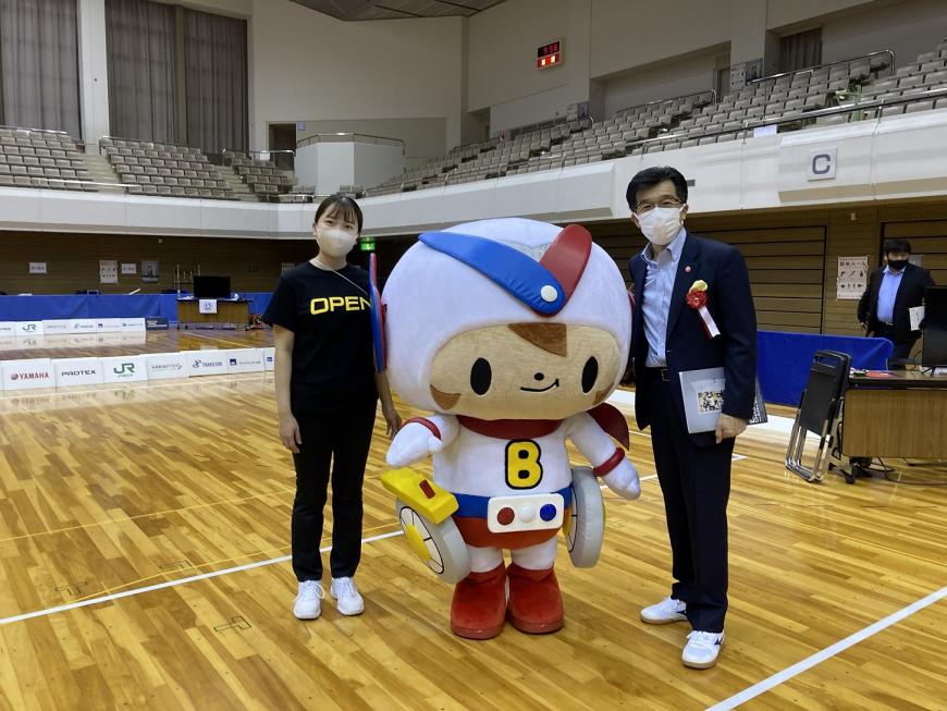 体育館で市長と女性の間にボッチャのキャラクター「ボッチャマン」が立っている写真