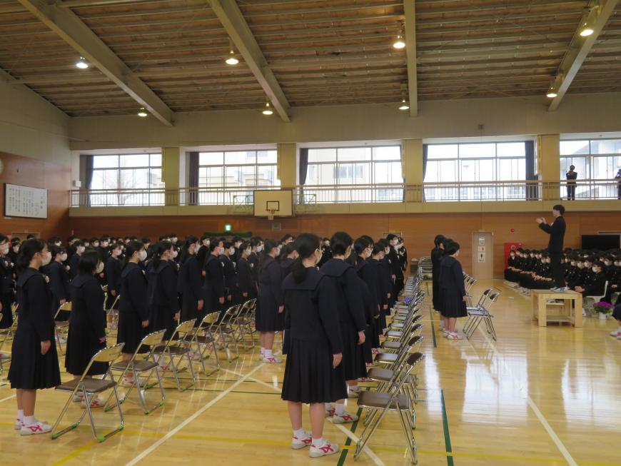 卒業生が在校生の方を向いて立ち、代表の生徒が台の上に立っている写真