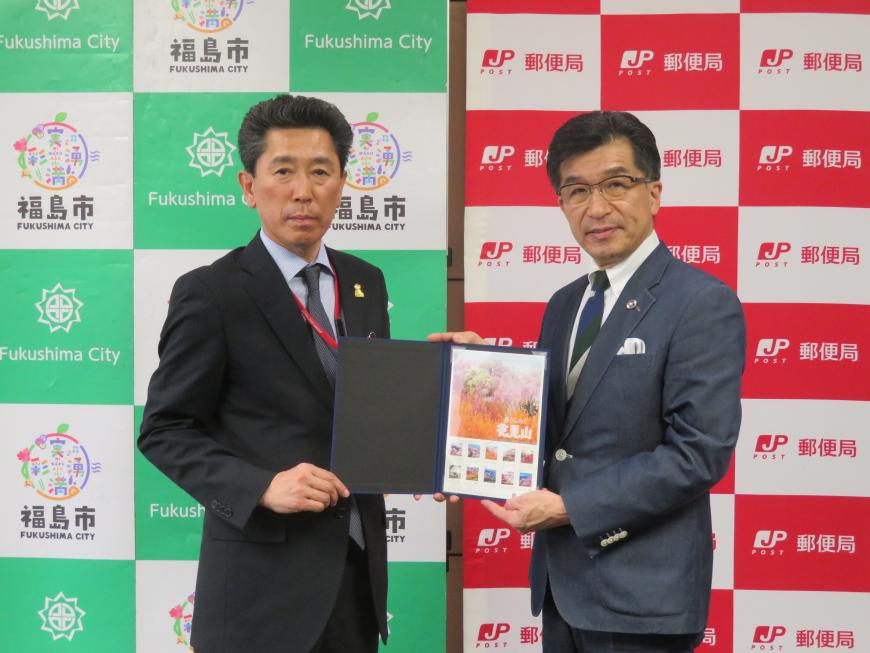 福島市と郵便局のバックパネルの前で、市長と男性でフレーム切手を持っている写真