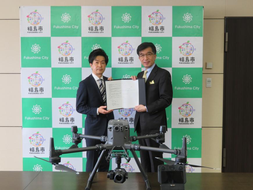 机に置かれたドローンの後ろで市長と男性で要望書を持っている写真