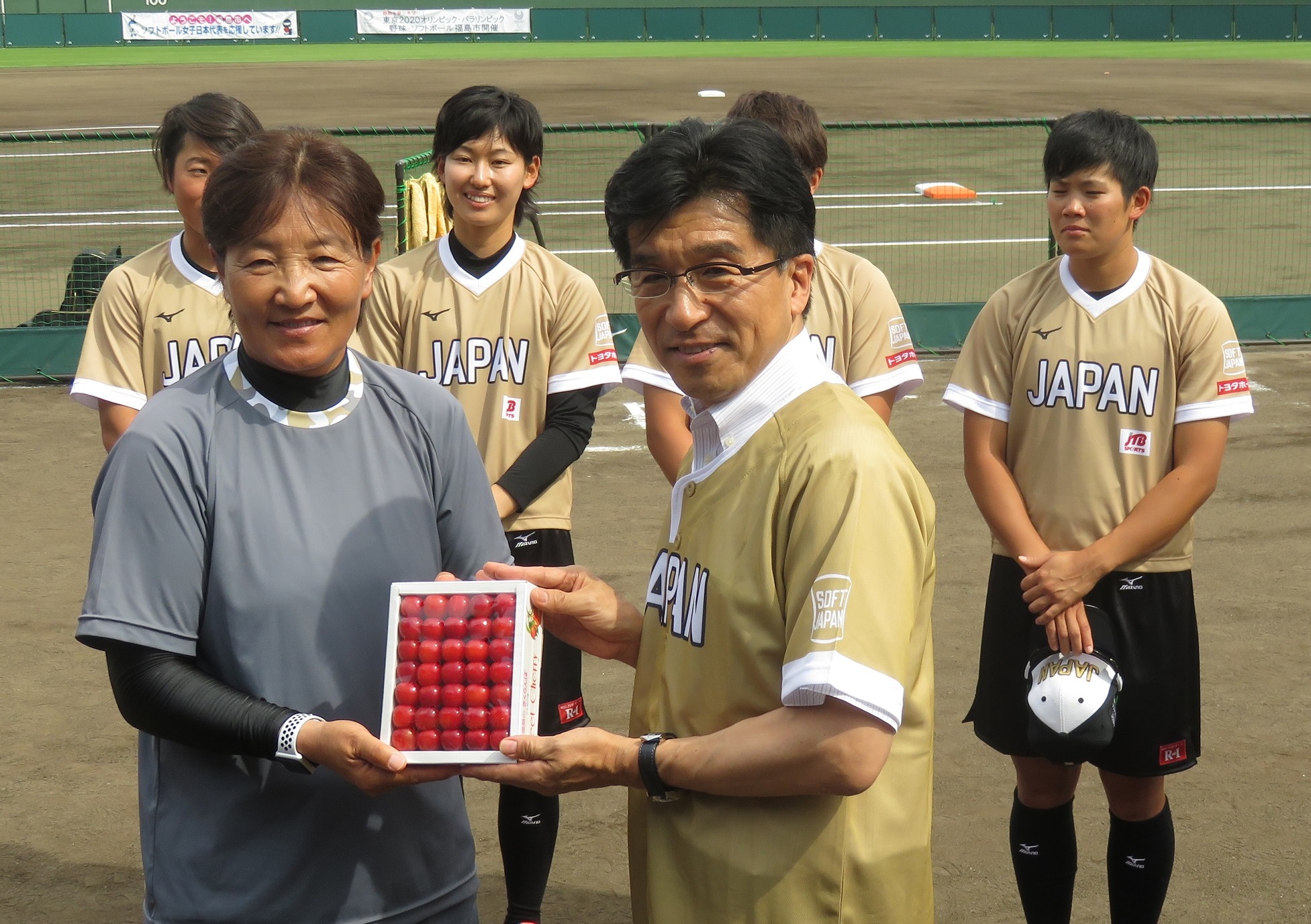 箱詰めされた真っ赤なさくらんぼを、ユニフォーム姿の市長が宇津木麗華監督へ手渡している写真