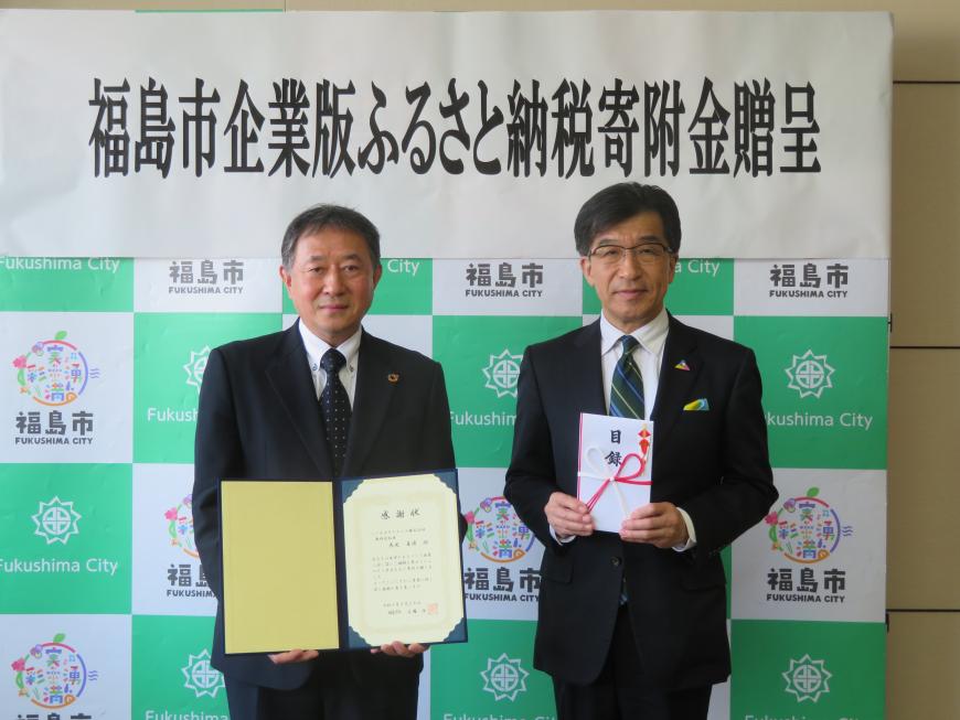 「福島市企業版ふるさと納税寄附金贈呈」の幕が貼ってあるバックパネルの前で、市長が目録を持ち、男性が感謝状を持って立っている写真