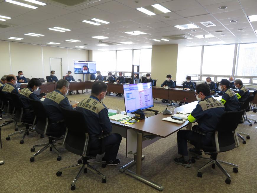 会議室前方のモニターにリモート参加者の顔が映され、背中に福島市災害対策本部と書かれた上着をきた関係者たちが口の字型に配置されたテーブルの席に座り話をしている様子の写真