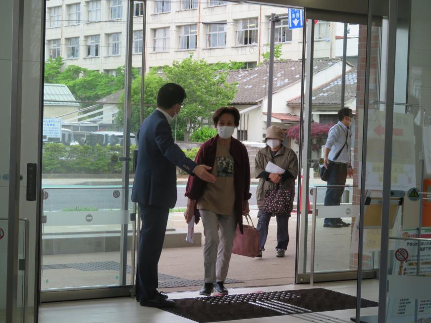 ガラスの自動ドアから女性が入るのを市長が手で中へ誘導している写真