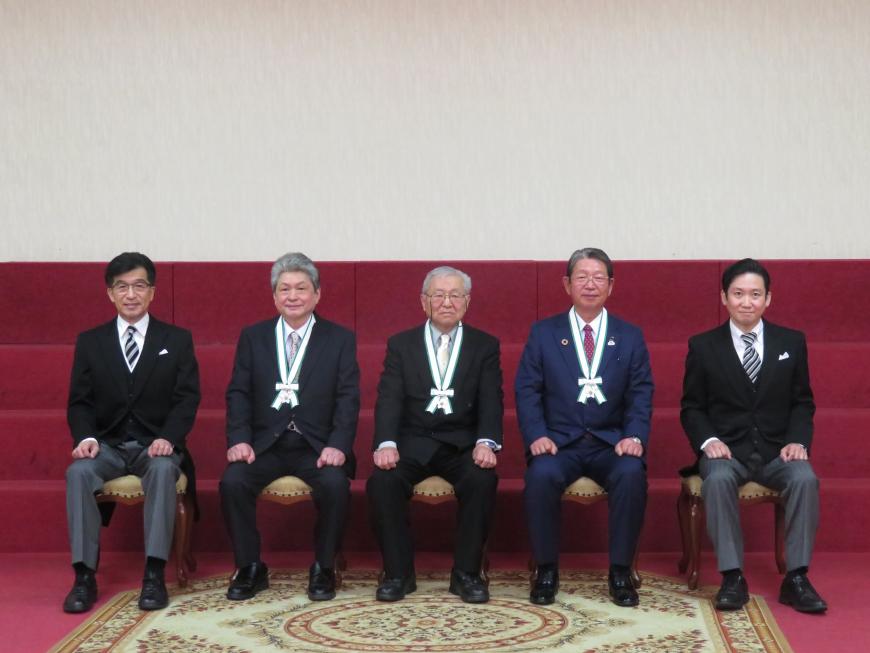 赤の絨毯が引いてある部屋で市長と関係者の間にメダルをかけた男性3名が座っている写真