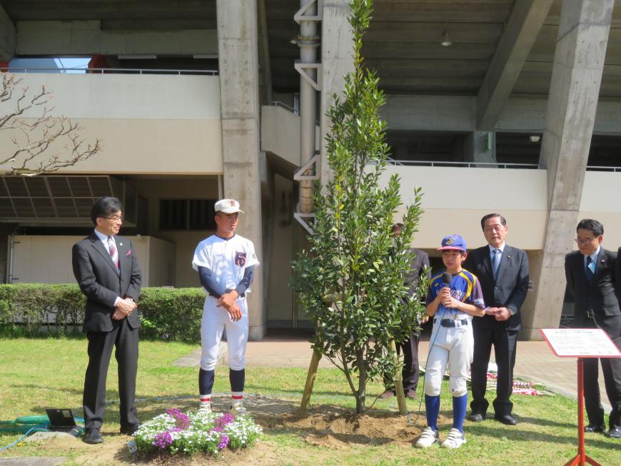 市長や関係者の方が見ている中、植樹した木の横でユニフォーム姿の男の子がマイクで話をしている写真