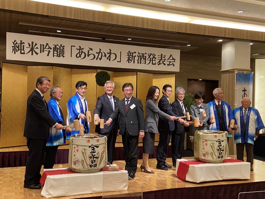 新酒発表会の会場で木槌を持った関係者たちが2つ並んだ酒樽の鏡開きをしている写真