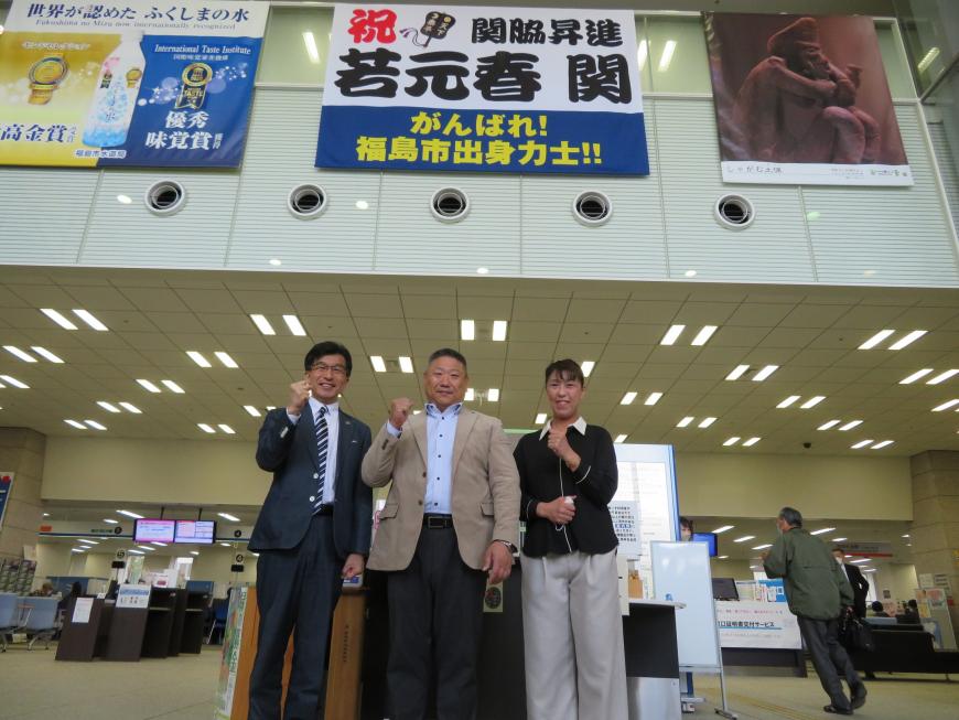若元春を応援する横断幕が掲示されている下で市長と男女各1名がガッツポーズをしている写真