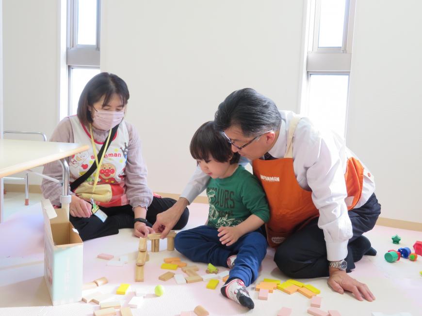 女性がみている中、市長と子供がおもちゃで遊んでいる写真