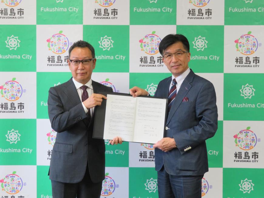 バックパネルの前で市長と男性で協定書を持っている写真
