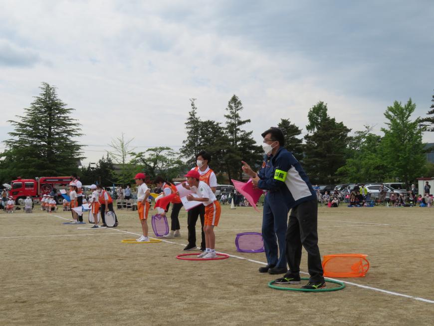 運動場に置かれた色の異なる輪の中に立っている児童と市長が、ジェスチャーをしている写真