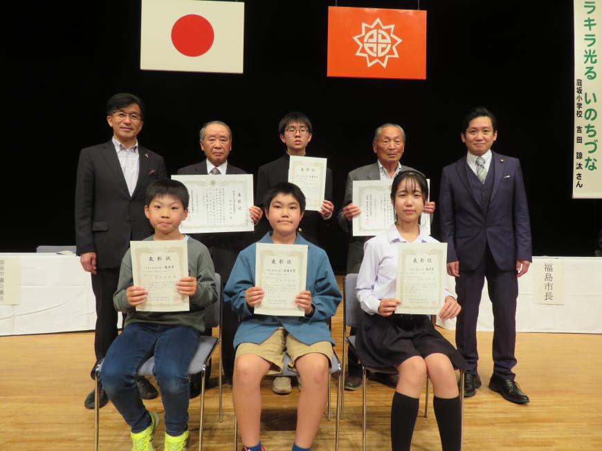 前列に表彰された3名が賞状を持って座り、後列に市長と関係者の間に表彰された3名が賞状を持って立っている写真