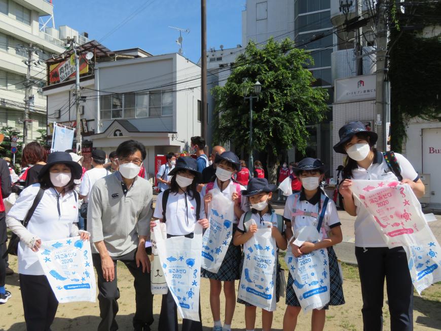 広場でビニール袋を持った女の子と女性ら6人と市長が並んでいる写真