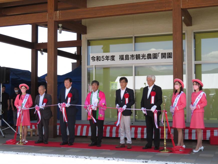 建物の前でミスピーチガールの間に市長を含む男性5名が立ちテープカットをしている写真