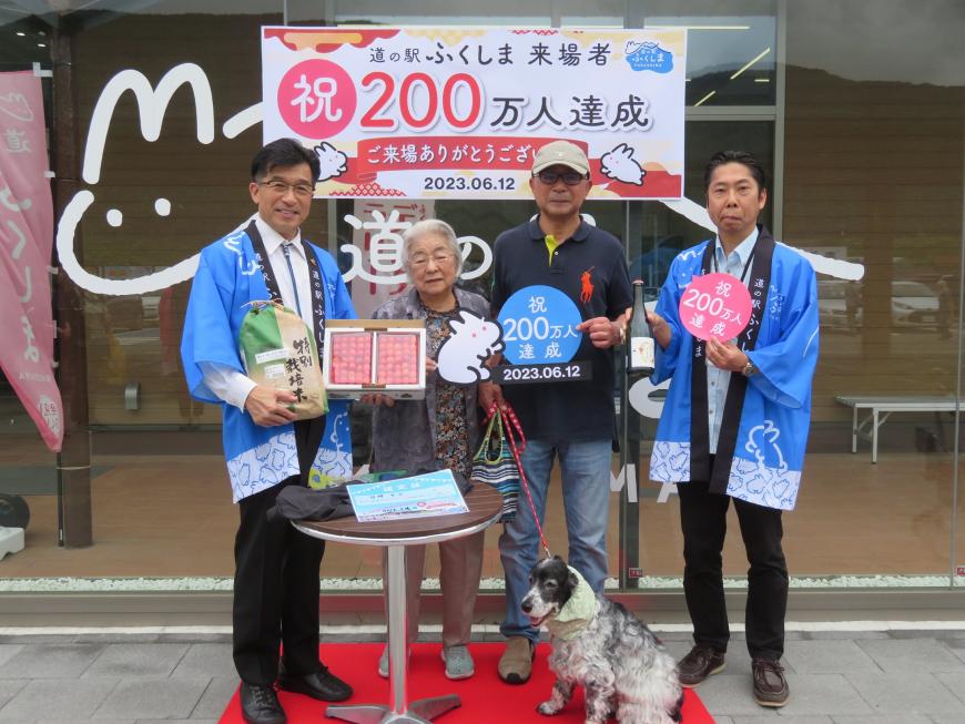 「200万人達成」の横断幕の前で法被を着た市長と職員の間に来場200万人目の女性と男性とペットの犬が立ち、記念品を持っている写真