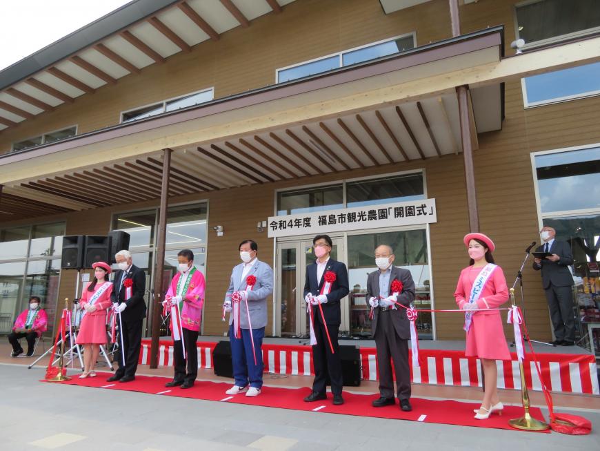 「令和4年度 福島市観光農園「開園式」」と書かれた横断幕が設置された建物の入り口前でレッドカーペットに立っている市長を含む男性5人でテープカットしている写真