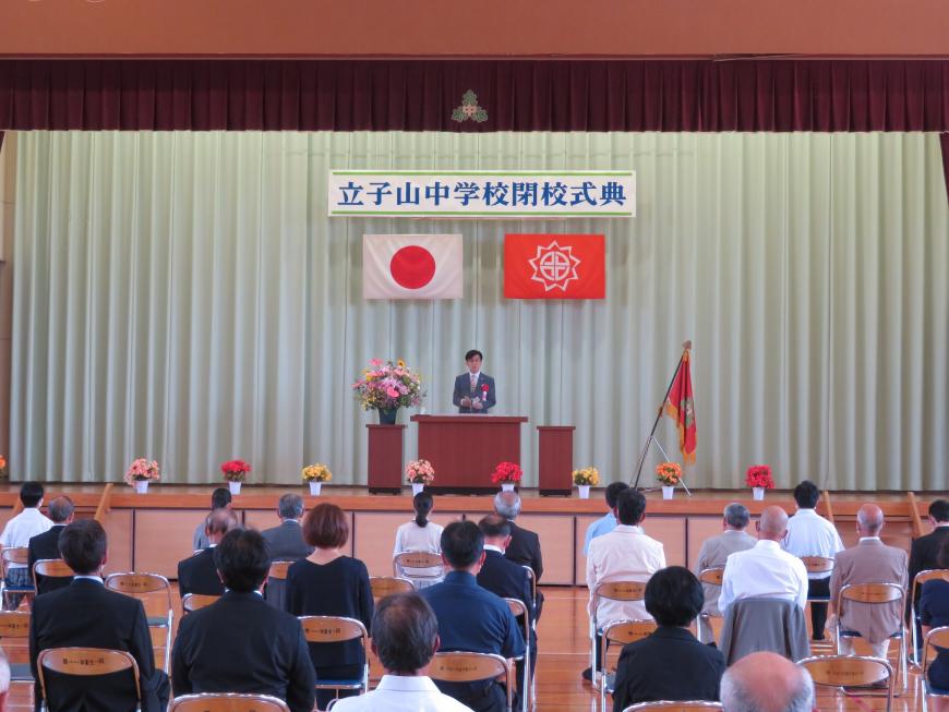 「立子山中学校閉校式式典」と書かれた横断幕飾られたステージの演台に立った市長が、並んだ椅子に座っている出席者たちに向かって話をしている写真