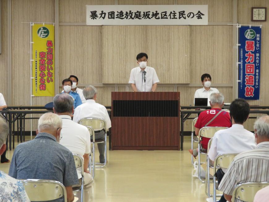 「暴力団追放庭坂地区住民の会」と書かれた横断幕の下で演壇に立ち話をしている市長と、並んだ椅子に座った参加者の方々の写真