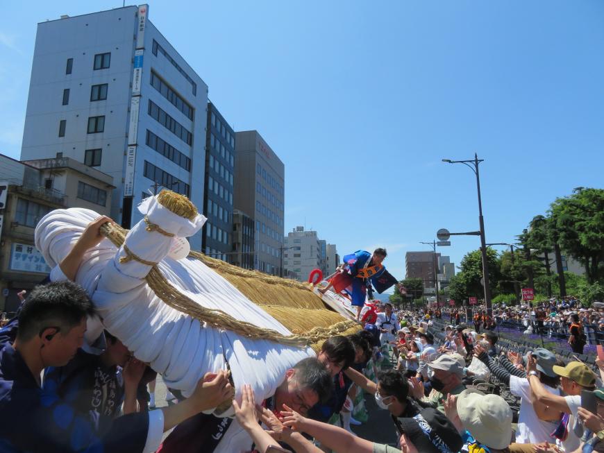 大勢の人で担いでいる巨大わらじを見て、沿道の人たちが触ろうとしたり、拍手したりしている写真