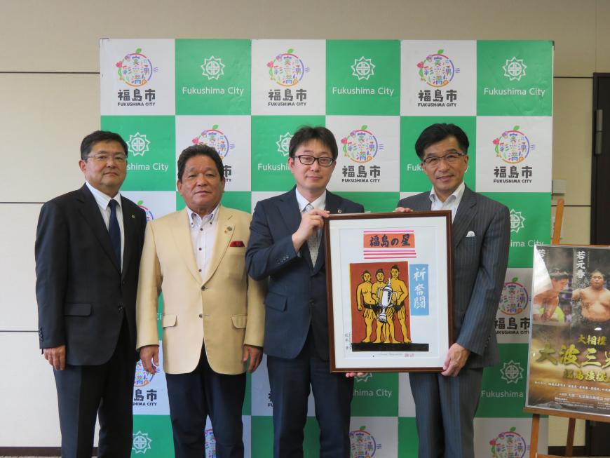 バックパネルの前で市長と男性で力士の版画を持ち、隣に男性2名が立っている写真
