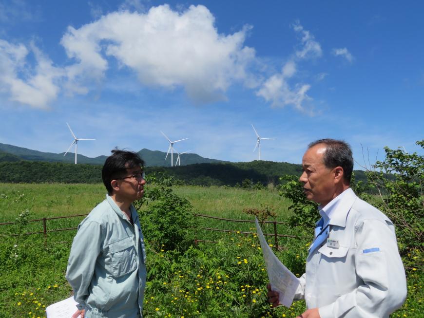 後方に風力発電が見えている緑豊かな場所で、市長と職員が話をしている写真