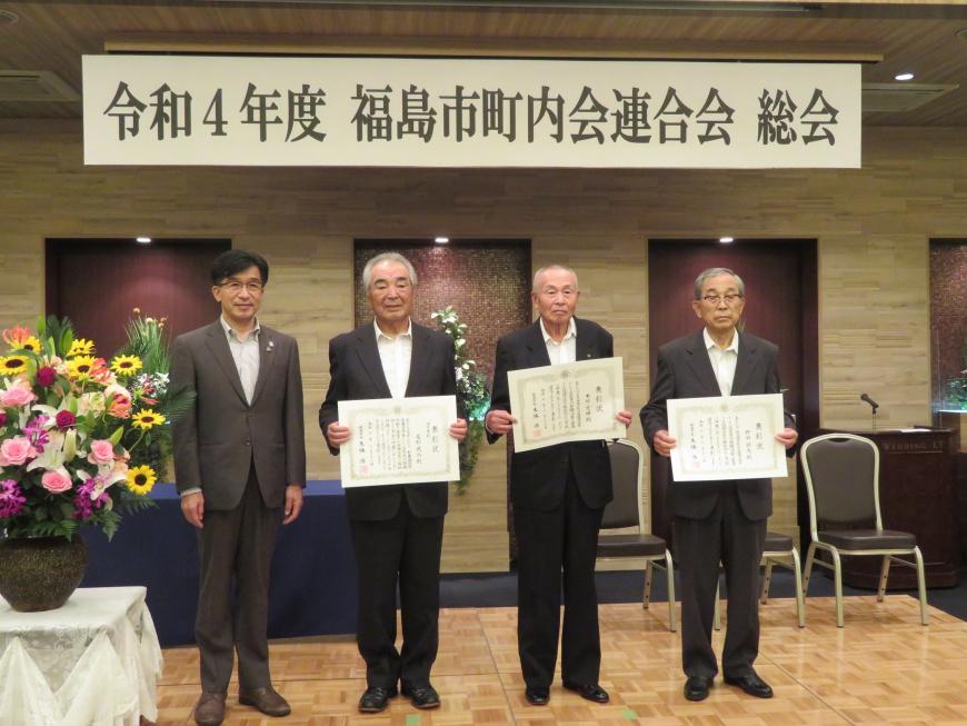 「令和4年度 福島市町内会連合会総会」のボードの下で、賞状を持った男性3人と市長が並んで立っている写真