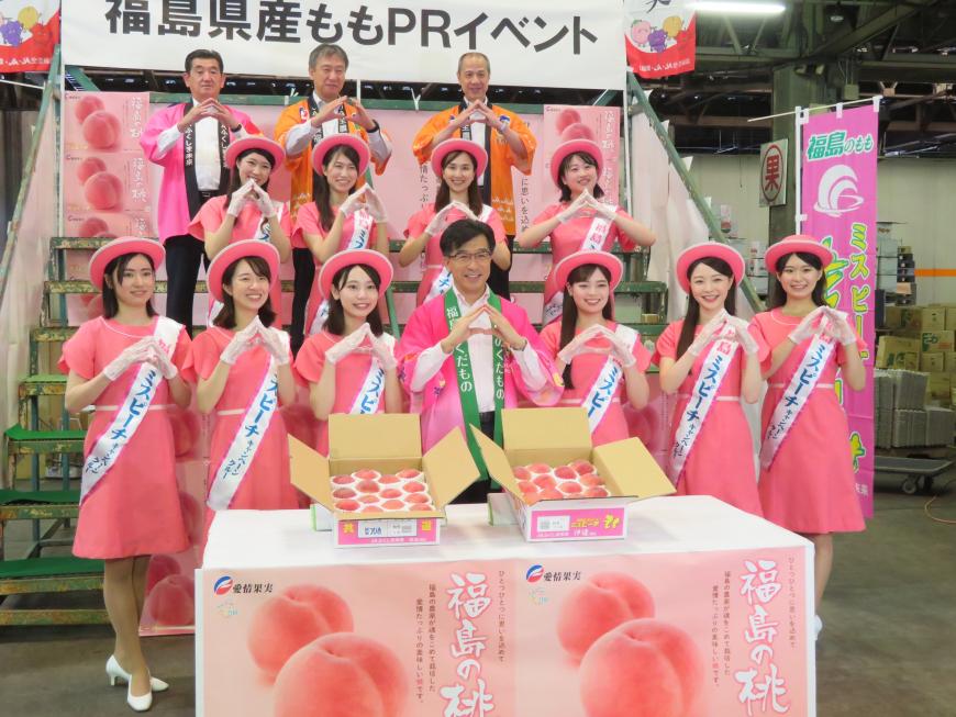 箱詰めの桃を置いた机の後ろに市長とミスピーチガールと関係者の方が両手でポーズをとって、ひな壇状に整列している写真
