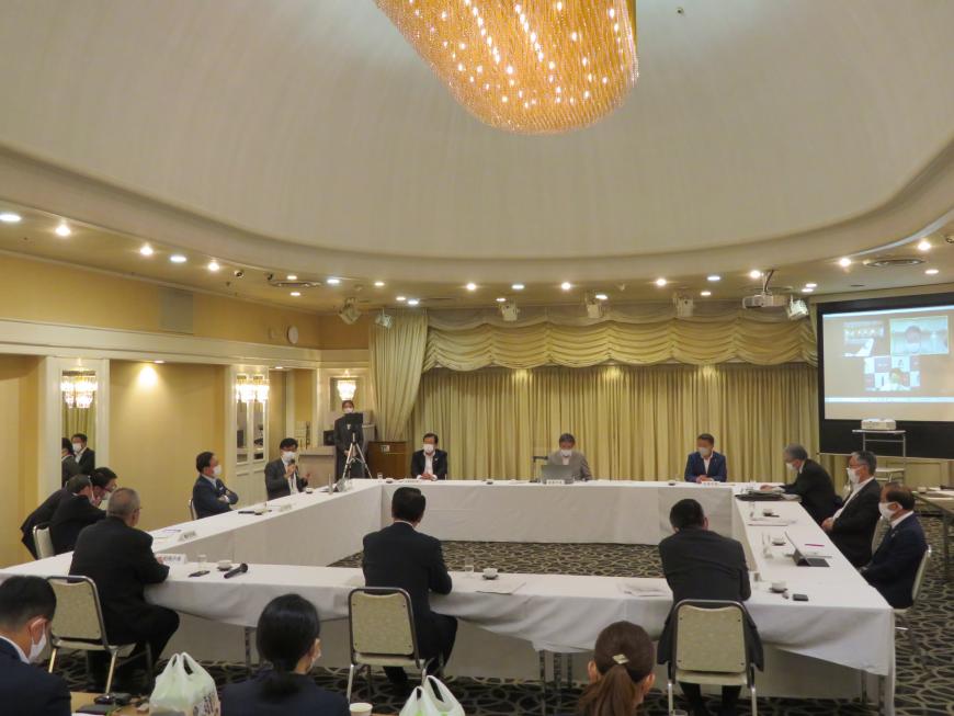 広い会場に白いテーブルクロスがかかったテーブルが口の字型に配置され、席に着いた出席者たちが会議を行っている様子の写真