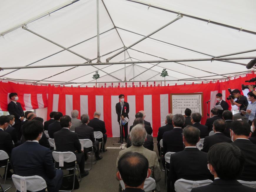 テント内に紅白幕が吊るされた会場に座っている参加者の前で、市長が話をしている写真