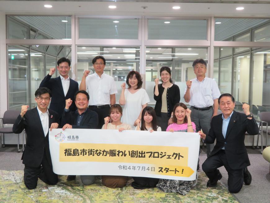 「福島市街なか賑わい創出プロジェクト」と書かれた横断幕を前列で市長と男性2人、女性3人で跪いて持ち、後列に男性3人、女性2人が立ち、皆でガッツポーズをしている写真