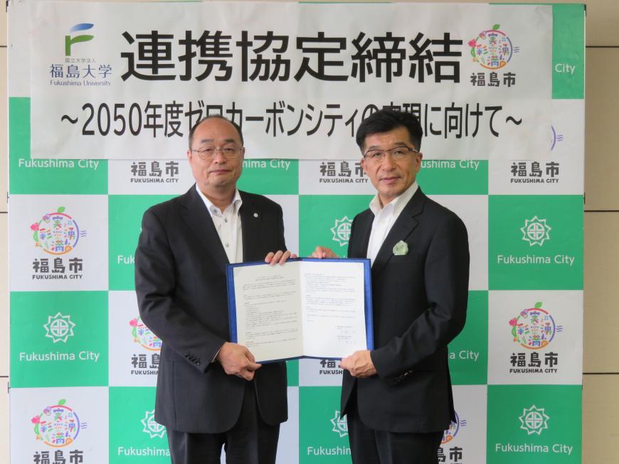 「連携協定締結」と書かれた横断幕が貼られたバックパネルの前で、市長と男性で協定書を持っている写真