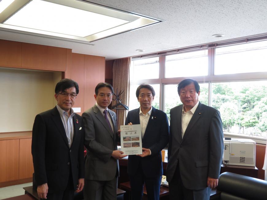 執務室内で男性2人で要望書を持っている横に市長と男性1人が立っている写真