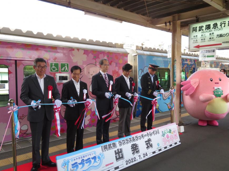 イラストが描かれた電車が停車しているホームで市長と駅長、他男性3人でテープカットをしている写真