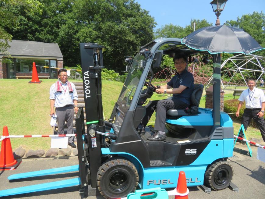 屋外で市長が青のフォークリフトに乗っている写真