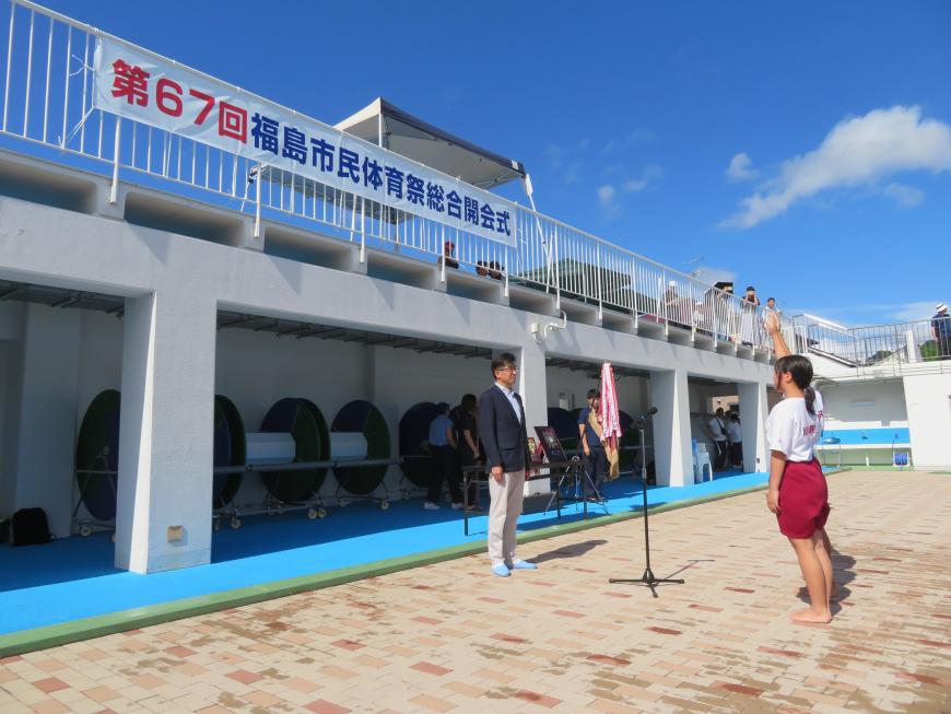 「第67回福島市民体育祭総合開会式」の横断幕が張られたプールサイドで体操服姿の女性が市長に選手宣誓をしている写真