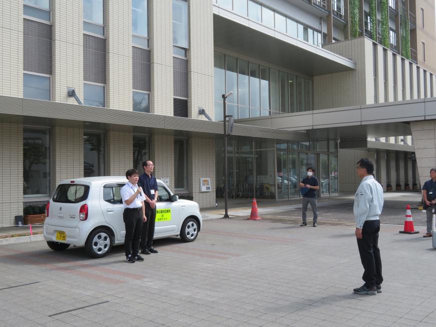 軽自動車の横に立っている2名の職員が向かい合っている市長へ話をしている写真
